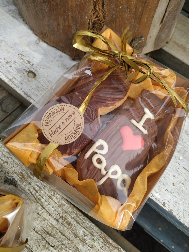 caja regalo para el día del padre compuesto de dos galletas de mantequilla: una corbata y un bigote, bañadas en chocolate. y debajo unas galletas de almendra y chocolate: kukiplanitas.